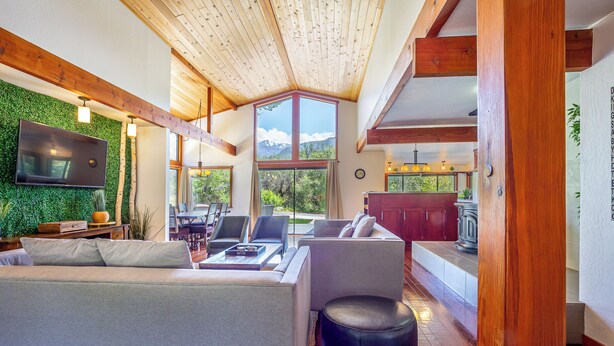 A modern living room with a large TV, comfortable seating, and a view of mountains through large windows. - Sequoia River House - 2 Decks on the River, close to SNP,  7 acres  (Three Rivers)