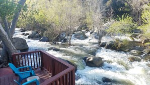 A wooden deck with blue chairs overlooking a fast-flowing river with rocks and trees. - Sequoia River House - 2 Decks on the River, close to SNP,  7 acres  (Three Rivers)
