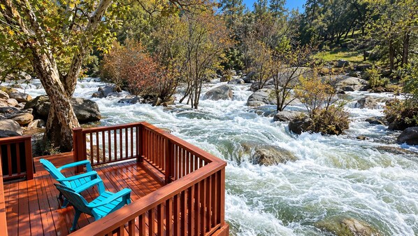 A wooden deck with blue chairs overlooking a turbulent river.