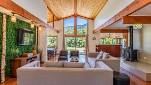 A spacious living area with a large sofa, wooden beams, a fireplace, and a view of the outdoors.