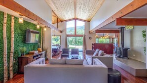 A spacious living area with a large window, wooden beams, a fireplace, and a green wall. - Sequoia River House - 2 Decks on the River, close to SNP,  7 acres  (Three Rivers)