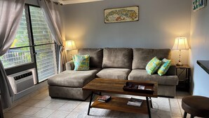 Una sala de estar con un sofá gris, dos almohadas estampadas, una mesa de centro de madera y dos lámparas.