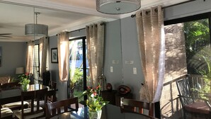Comedor con mesa, sillas, lámpara colgante y ventanas amplias con cortinas.
