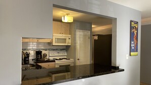 Cocina compacta con microondas, estufa y lavaplatos, además de un pequeño bar con taburetes.