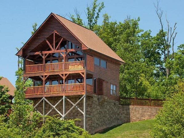 Une cabane en rondins à deux étages, dotée d’un balcon à l’étage supérieur et entourée de verdure.