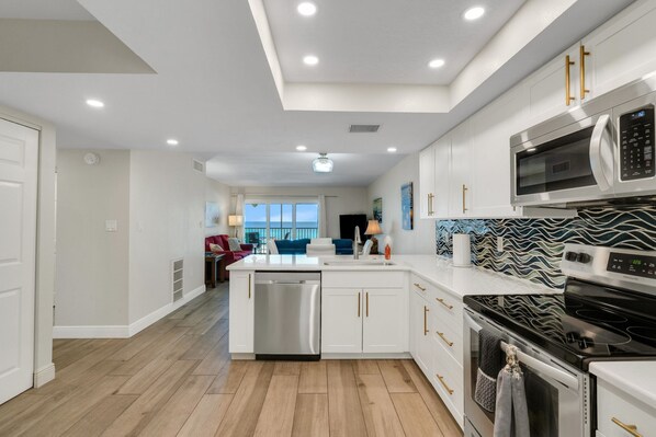 A modern kitchen with white cabinetry, stainless steel appliances, and a wooden floor.