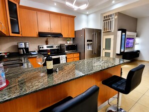 A modern kitchen with granite countertops, stainless steel appliances, wooden cabinets, and a bar area with seating. - CASA BORINQUEN VACATION RENTAL (Aguadilla)