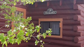 A rustic log cabin with a wooden exterior, a window with a small wooden frame, and a sign reading "120 The Madison". - Rustic Charm Meets Modern Comfort, Steps from Yellowstone's West Entrance (West Yellowstone)