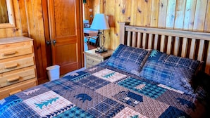 A wooden-paneled room with a bed, dresser, and a door leading to another room. - Rustic Charm Meets Modern Comfort, Steps from Yellowstone's West Entrance (West Yellowstone)