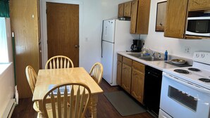 A compact kitchen with wooden cabinets, a white refrigerator, a microwave, a stove, and a sink. - Rustic Charm Meets Modern Comfort, Steps from Yellowstone's West Entrance (West Yellowstone)