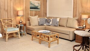 A cozy living room with a wooden paneled wall, a beige sofa, a glass coffee table, and two wicker chairs. - Perfect for multi-family gatherings! (Oak Island)