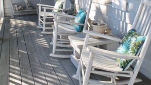 A porch with white rocking chairs, a ceiling fan, and a wall-mounted lantern. - Perfect for multi-family gatherings! (Oak Island)