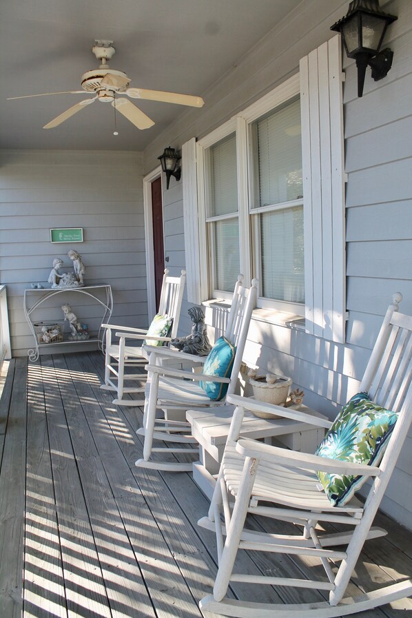 A porch with white rocking chairs, a ceiling fan, and a wall-mounted lantern.