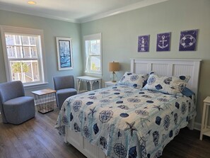 Une chambre à coucher comprenant un lit, une chaise, une table de chevet et une fenêtre décorée d’œuvres d’art.