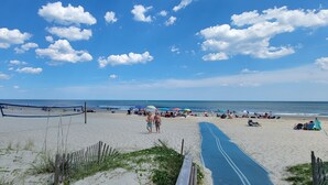 Una playa con una red de voleibol, sombrillas y gente.