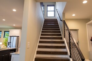 Stairs lead to an upper level with a window, flanked by white walls and a black railing.