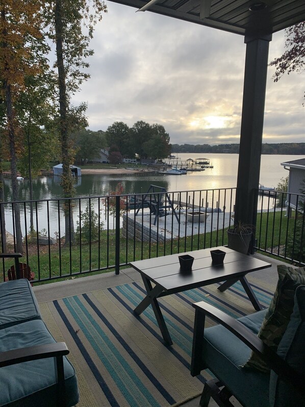Relax by the serene lake with a table and chairs on the deck, surrounded by a grassy lawn and trees.
