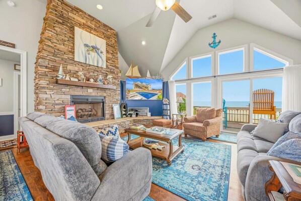 A spacious living room with a stone fireplace, large windows, and a view of the ocean.