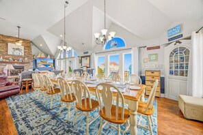Uma sala de jantar espaçosa com teto alto, lareira e vista para o mar.