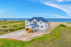A two-story house with a balcony, a deck, and a view of the beach and ocean.