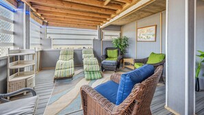 A covered outdoor seating area with wicker furniture and a wooden ceiling.