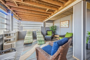 A covered outdoor seating area with wicker furniture and a wooden ceiling.