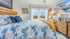 A bedroom with a bed, a ceiling fan, a dresser, and a view of the outside.