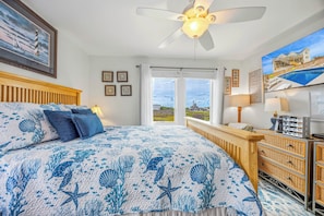 A bedroom with a bed, a ceiling fan, a dresser, and a view of the outside.