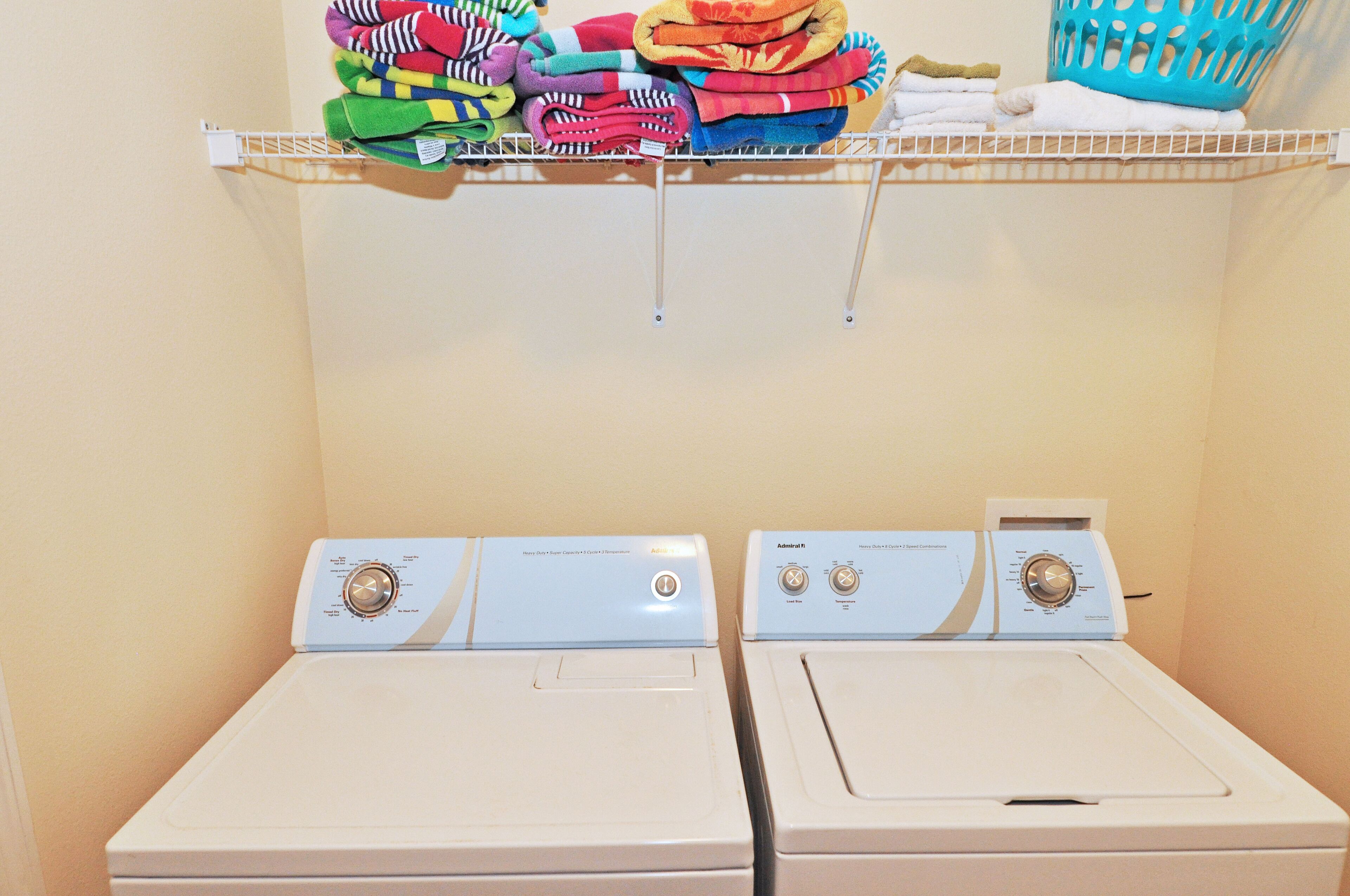 A laundry area with two white front-loading washing machines and a shelf above holding folded towels.