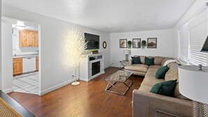 Ein modernes Wohnzimmer mit Sofa, Couchtisch und Kamin. Durch einen offenen Durchgang ist eine Küche erkennbar.