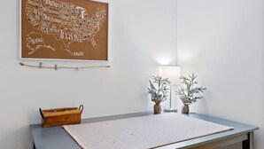Ein Zimmer mit einer Korkpinnwand mit einer Karte der USA, einem kleinen Holznachttisch, einer großen gewebten Matte und zwei Blumentöpfen mit einer Lampe.