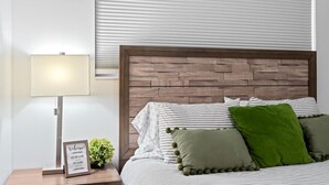 Ein ordentlich bezogenes Bett mit gestreifter Bettwäsche und dekorativen Kissen, eine Nachttischlampe und ein Willkommensschild auf dem Nachttisch.