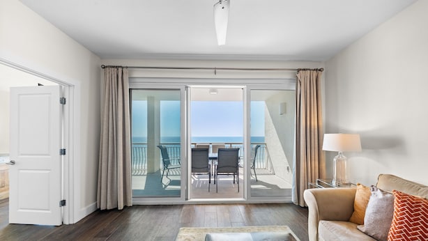 A hotel room with a balcony, a sofa, a table, and a lamp.
