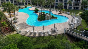 A resort with a large, winding pool surrounded by lounge areas and palm trees.