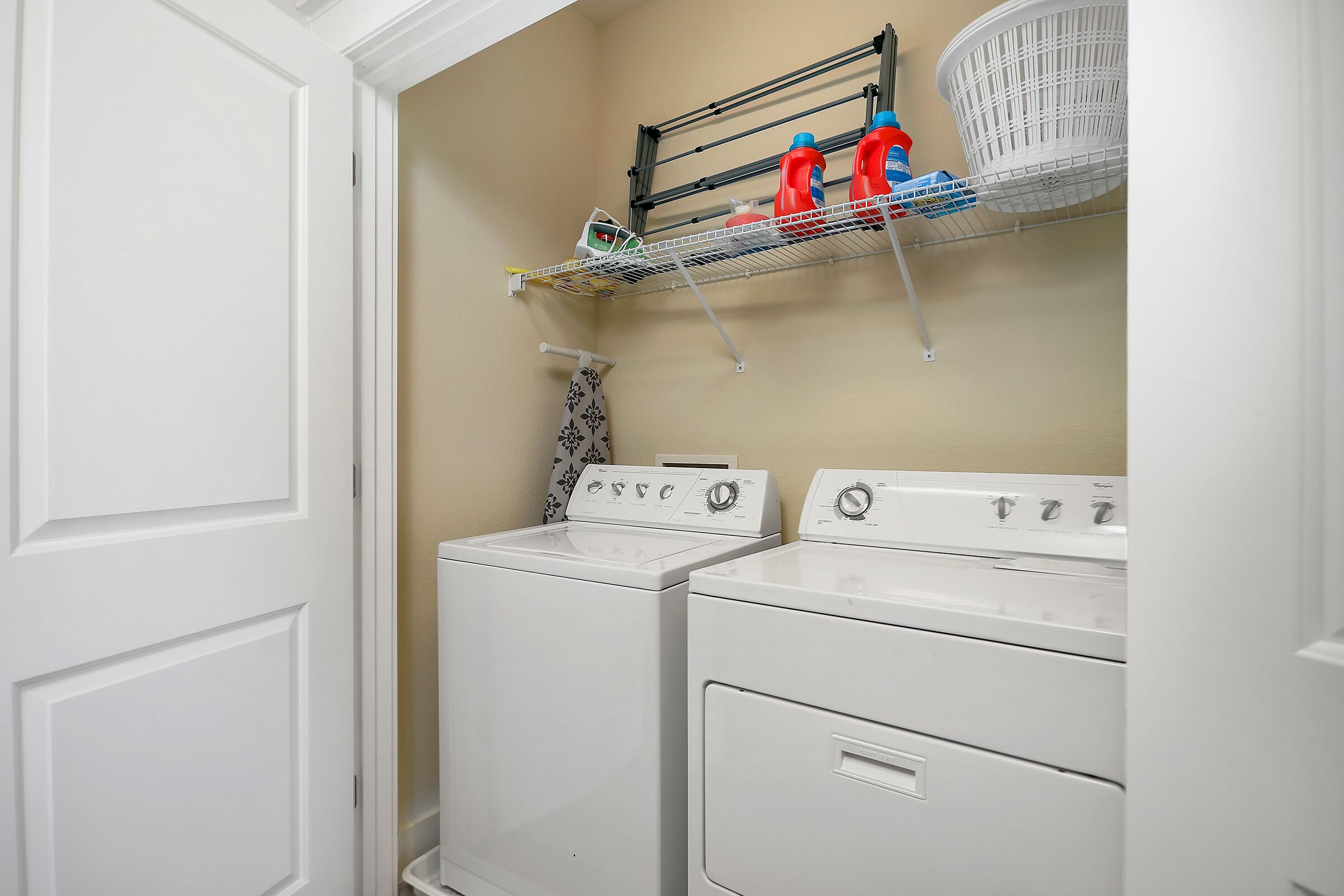 A laundry room with two stacked washers and dryers, a drying rack with laundry, and a basket.