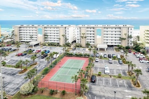 A hotel with multiple floors, a parking lot, and a tennis court.