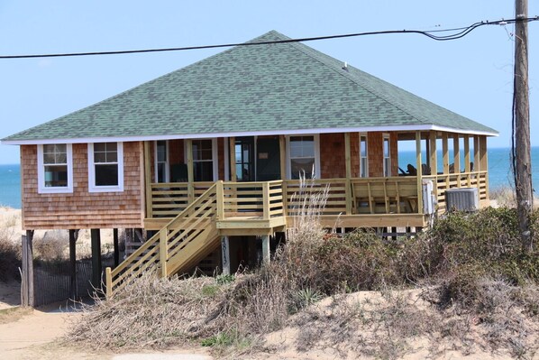 Une maison de plage en bois, avec un toit vert, une terrasse en bois et un petit porche.