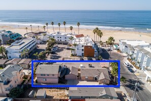 A coastal residential area with beachfront properties, including a two-story house with a sloped roof and a smaller attached structure, surrounded by palm trees and a beach in the background. - LOCATION!!!  7 Bedrooms - VIEW - Steps to Sand+Ocean+Pier+Downtown PISMO BEACH! (Pismo Beach)