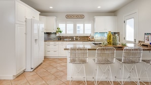 A kitchen with white cabinets, a central island with bar stools, a sign reading "BEACH HOUSE", and a large window with blinds. - LOCATION!!!  7 Bedrooms - VIEW - Steps to Sand+Ocean+Pier+Downtown PISMO BEACH! (Pismo Beach)