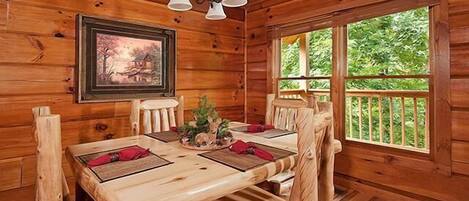 Ein Holzblockhaus-Innenraum mit einem Esstisch, Stühlen, einer Kandelaber und einem Bild an der Wand.