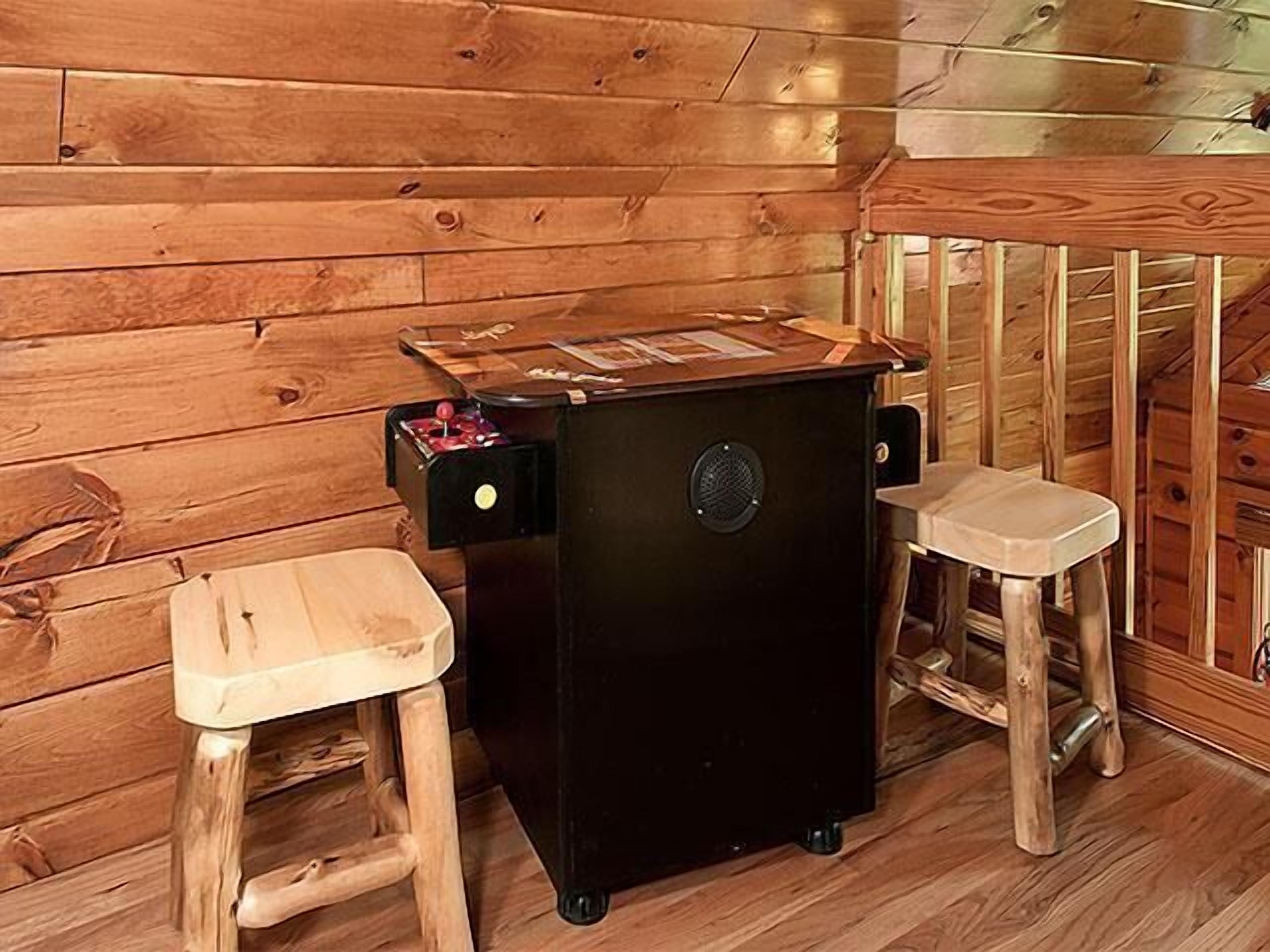 Interior de una cabaña de madera con un calefactor negro, dos taburetes de madera y una pequeña mesa.