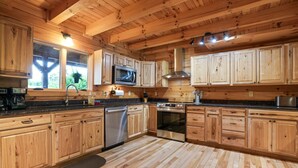 A kitchen with wooden cabinets, a stainless steel dishwasher, an oven, and a microwave. - Premium Hocking Hills Group Lodge 8BR 5.5Ba Hot Tub, Pond, Starlink, Game Room (Logan)