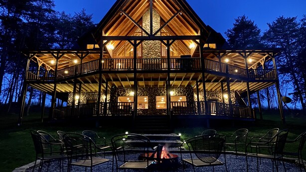 A multi-level wooden cabin with a stone facade, outdoor seating, and a fire pit. - Premium Hocking Hills Group Lodge 8BR 5.5Ba Hot Tub, Pond, Starlink, Game Room (Logan)