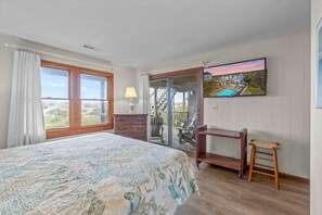 A bedroom with a large bed, a desk, a chair, a TV, and a view of a pool and house through a glass door. - Oceanfront, Dog Friendly Home with Private Pool, Hot Tub, and Beach Sunrises! (Salvo)