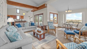 A spacious living room with a grey sofa, a wooden coffee table, wicker chairs, and a view of the beach through large windows. - Oceanfront, Dog Friendly Home with Private Pool, Hot Tub, and Beach Sunrises! (Salvo)