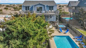 A beachfront house with a pool, deck chairs, and a surfboard sign. - Oceanfront, Dog Friendly Home with Private Pool, Hot Tub, and Beach Sunrises! (Salvo)
