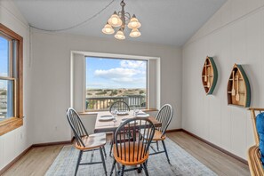 A dining room with a large window, a chandelier, and wooden chairs. - Oceanfront, Dog Friendly Home with Private Pool, Hot Tub, and Beach Sunrises! (Salvo)