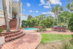 A backyard with a swimming pool, red lounge chairs, and a brick staircase leading to a house.