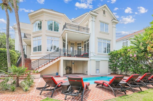 A large, two-story house with a pool, outdoor seating, and a staircase leading to a balcony.