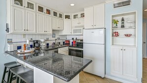 Una cocina con armarios blancos, encimera de granito y refrigerador.